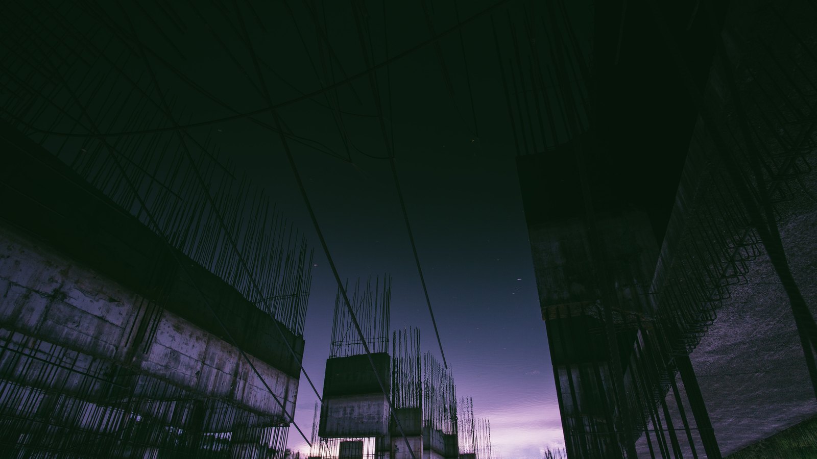 An unfinished concrete building frame with exposed reinforcing bars at dusk.