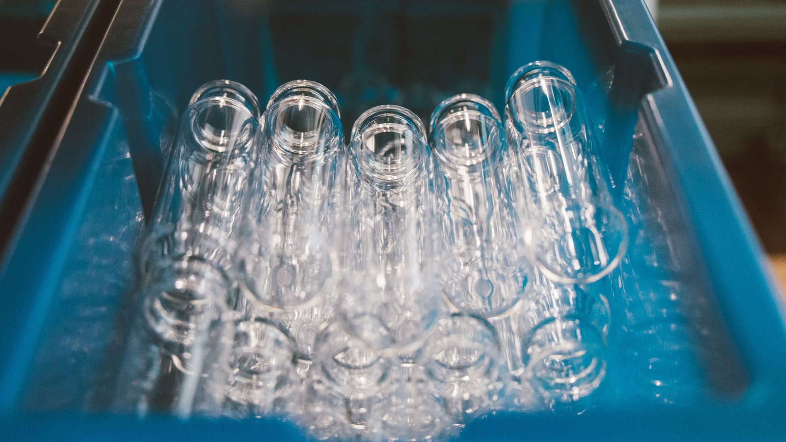A close photograph of about a dozen clear glass tubes lying with their open ends towards the camera in a blue plastic crate, lit from above, carrying no label or lettering and with nobody in the frame.