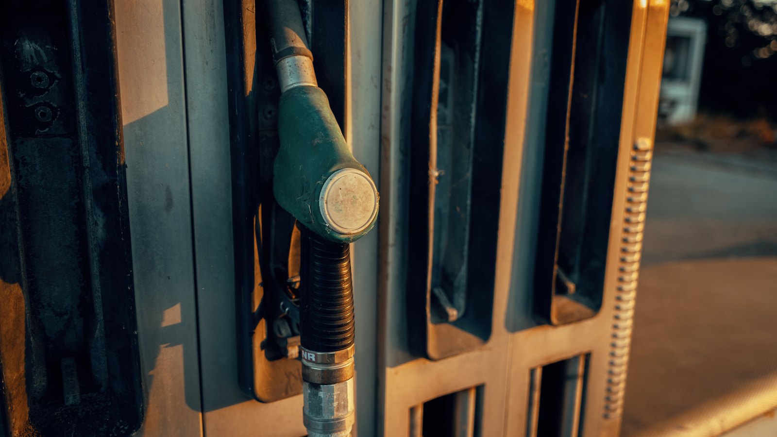A green fuel nozzle resting in its holster on a filling station dispenser, lit by low evening sun.