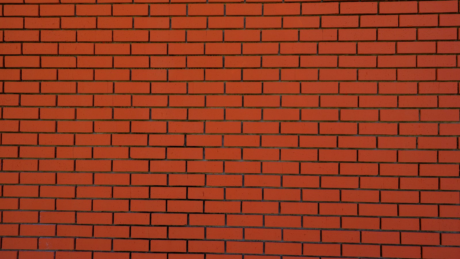 A red brick wall filling the frame, laid in running bond, with courses of identical bricks stepping half a length at each row and thin dark mortar joints between them.