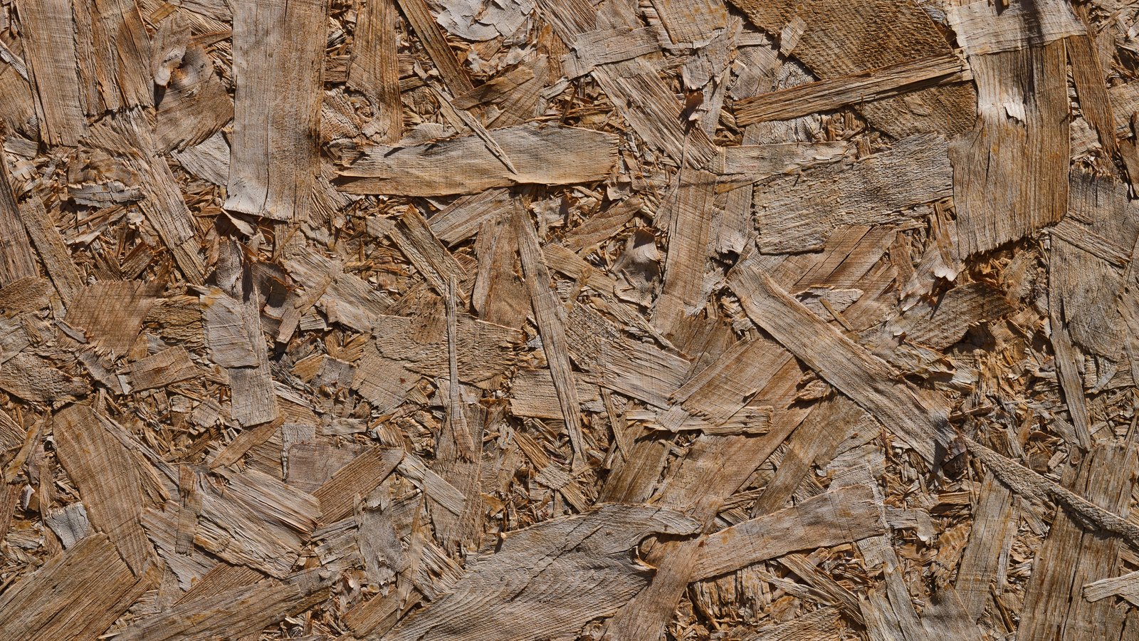 A close photograph of an oriented strand board panel, its surface a dense random overlap of flat pale timber flakes pressed together and filling the whole frame. No text, lettering, brand mark, tool, person or place is in view.
