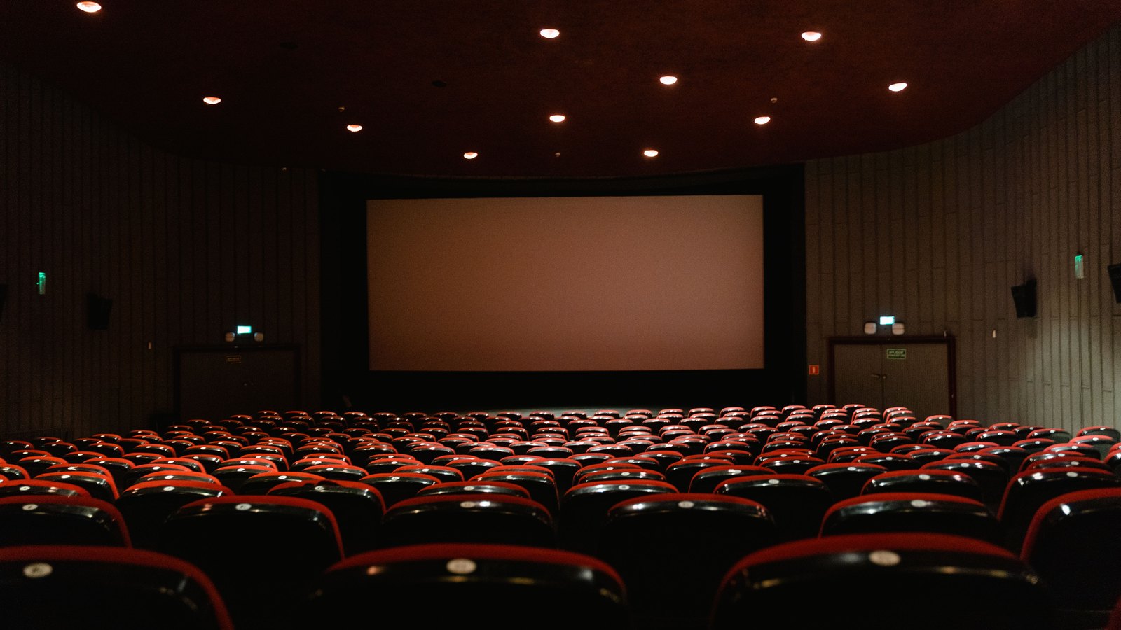 Rows of empty red seats face a blank screen in a movie theater, not the Mercato cinema.
