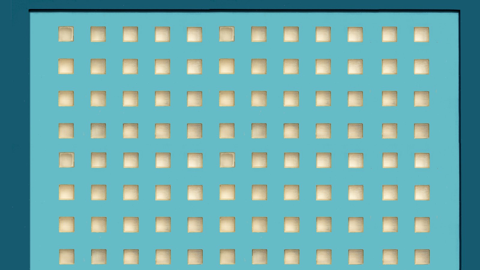 A photograph of a flat teal painted panel filling almost the whole frame, pierced by eight even rows of small square recessed apertures in regular columns, each aperture catching a warm pale light, with the edge of the panel visible along the top and left. No text, brand mark, person or place is in view.