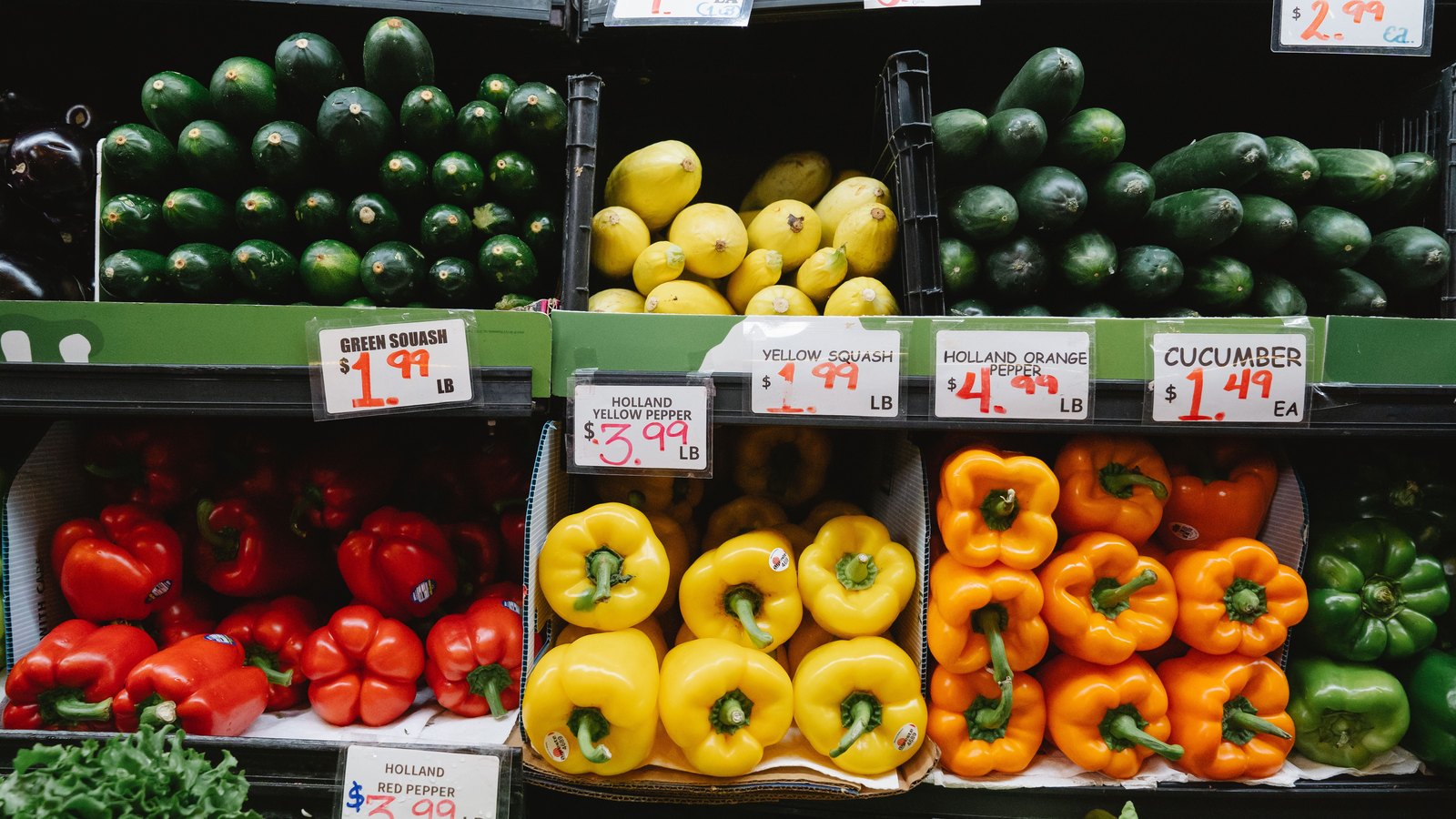 Colorful vegetables and handwritten price cards fill a grocery store produce display, not a photograph of this event.