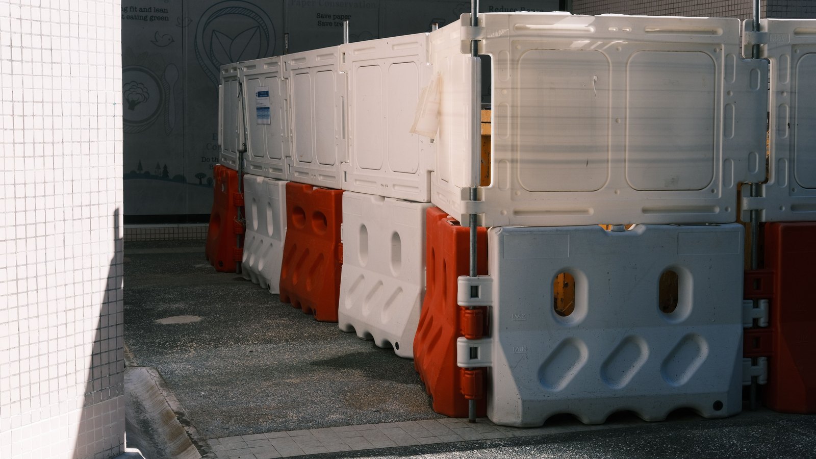 Red and white plastic traffic barriers line a paved access lane, not a photograph of the Alico Road closure.