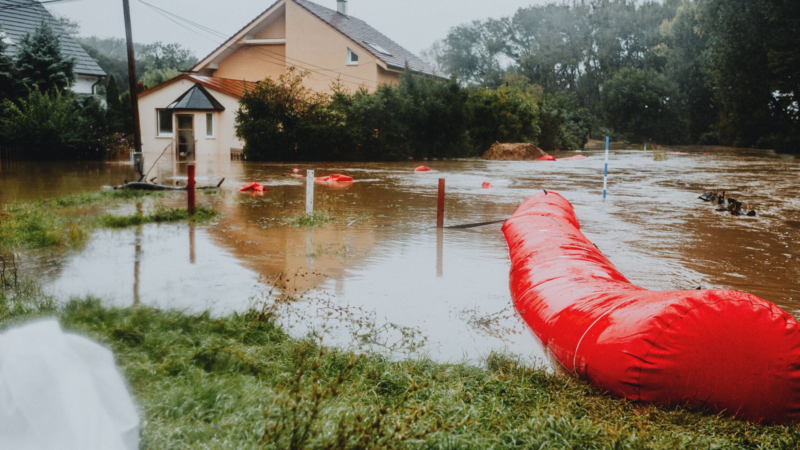 A red temporary flood barrier curves through high water beside generic homes under an overcast sky. No person, sign, logo, address or identifiable landmark appears. A stock photograph, not a photograph of this event.