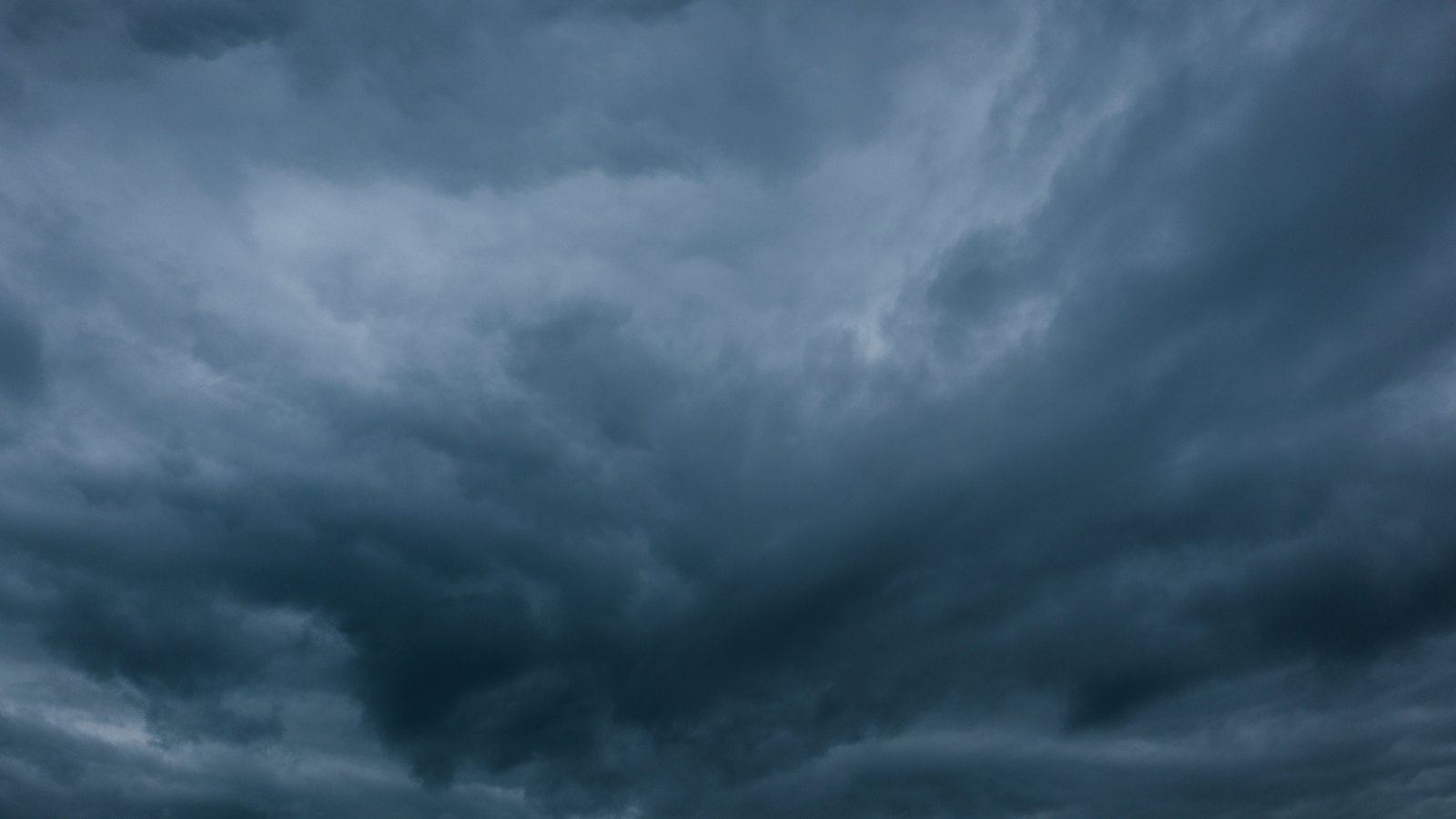 A dense mass of dark blue grey storm cloud filling the entire frame, layered and torn through the middle, with no horizon, ground, building or aircraft anywhere in view. No lettering is present.