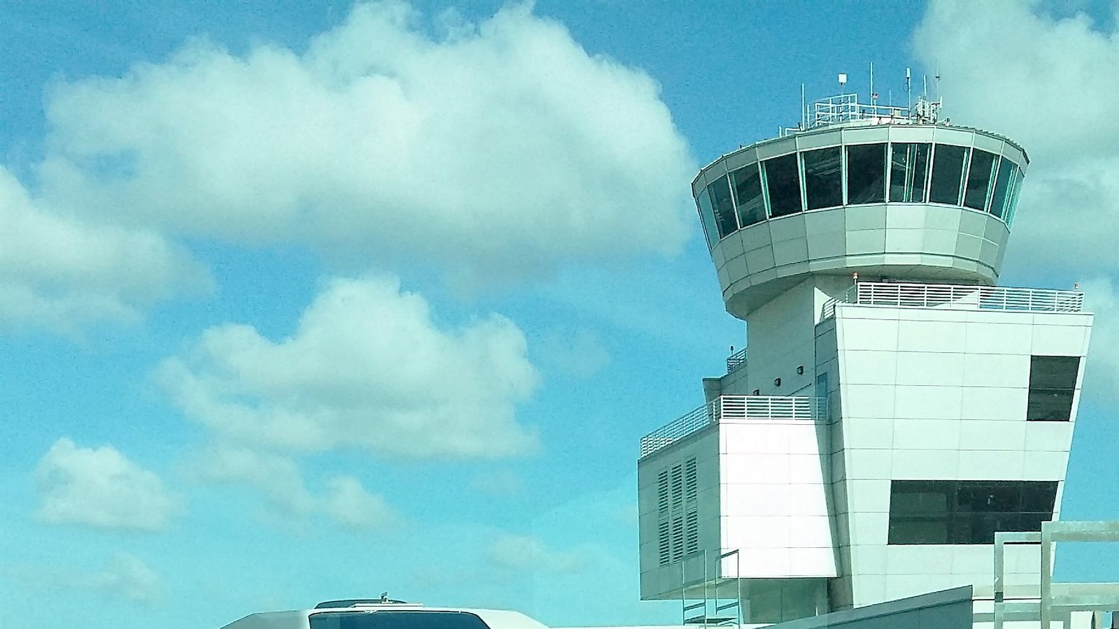 The Miami International Airport control tower against a blue sky, with the roof of a Skytrain in the foreground.