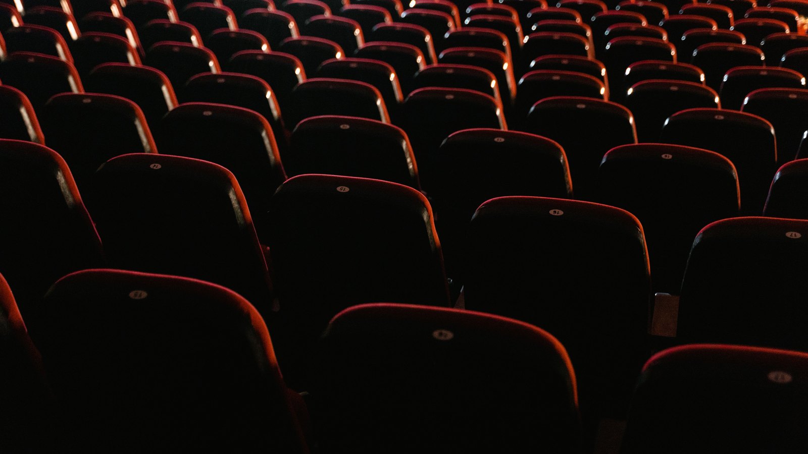 Rows of empty red seats in a dark cinema auditorium.