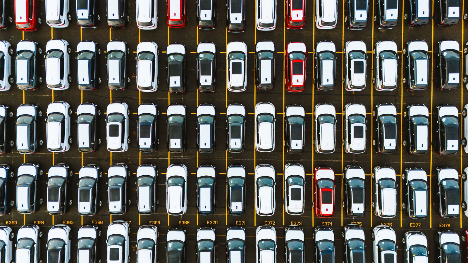 Rows of cars parked in a dealership lot, viewed from above.
