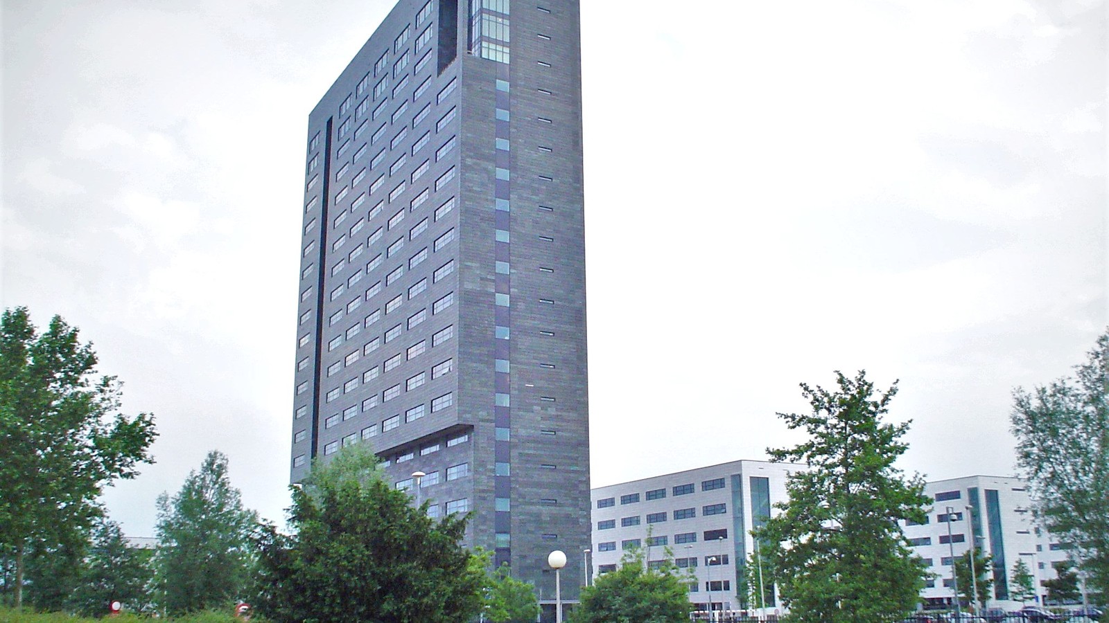 The ASML headquarters tower in Veldhoven, Netherlands, rises above trees and lower office buildings.
