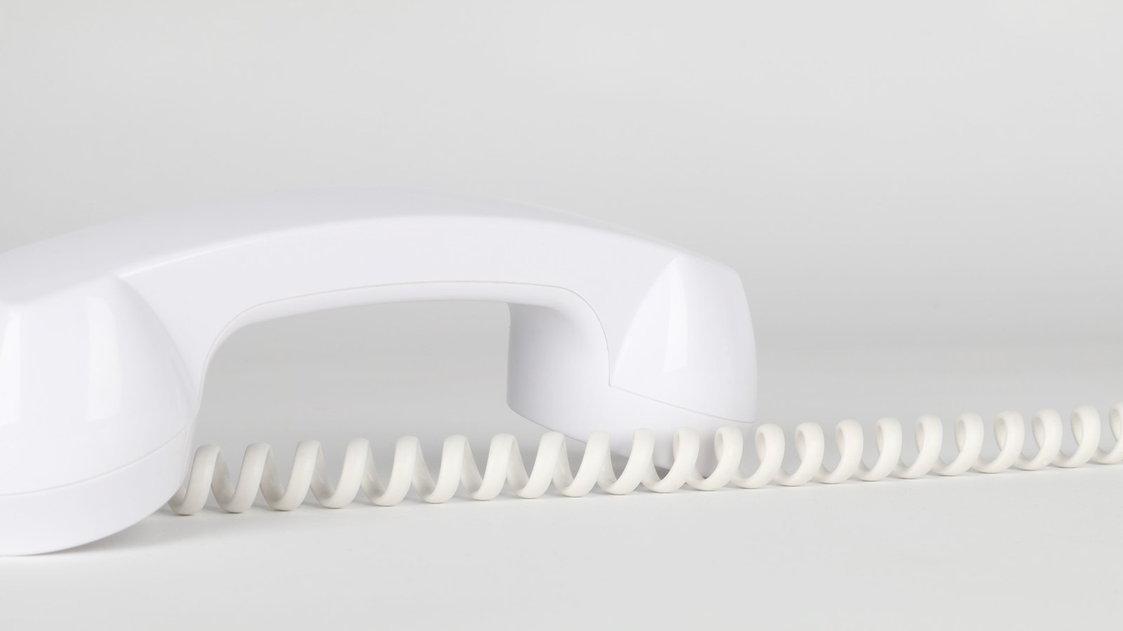 A white corded telephone receiver and coiled cable on a plain white surface, shown as a stock photograph rather than the actual incident.