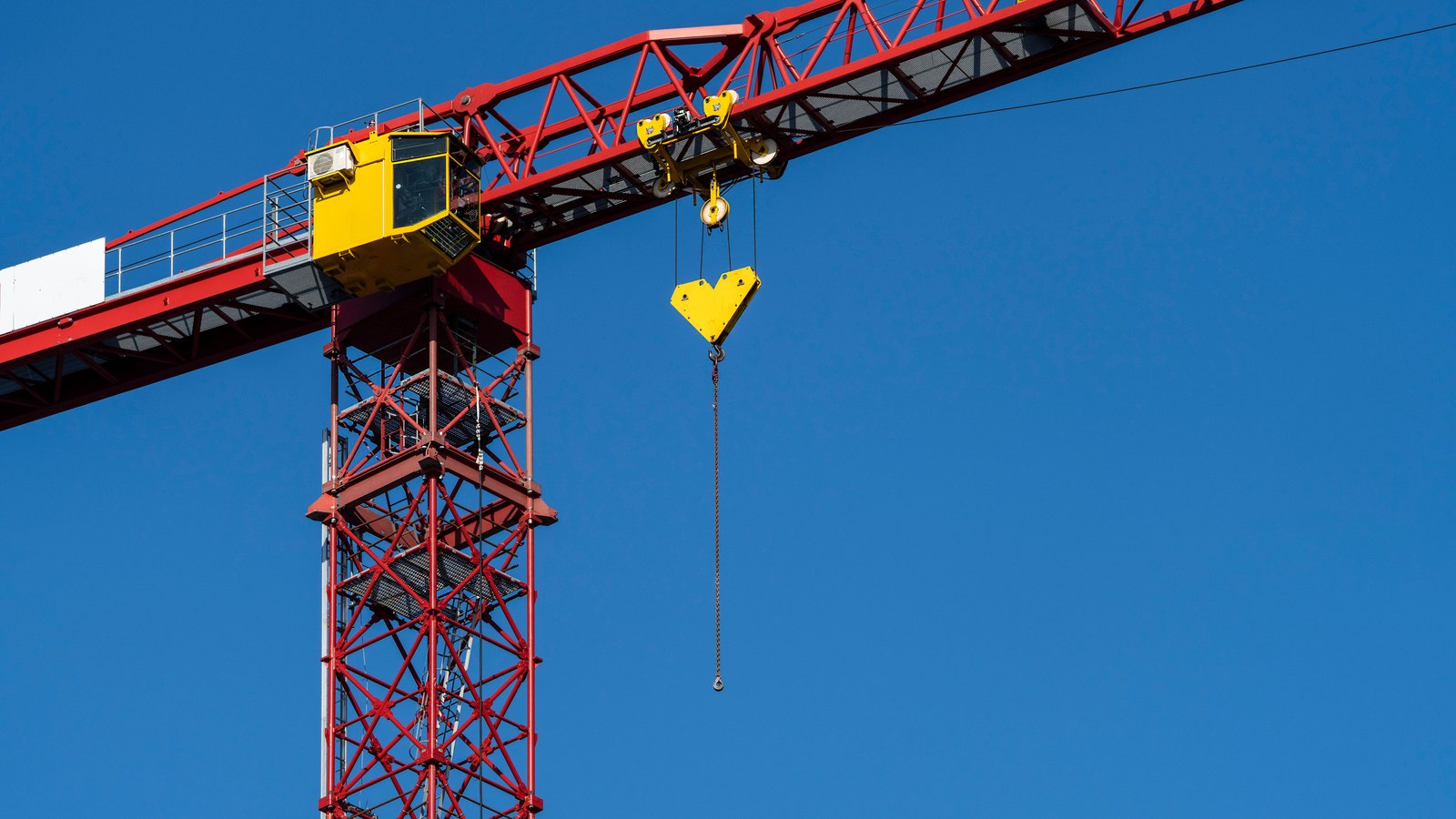 A red tower crane with a yellow cab and an empty hook stands against a clear blue sky.