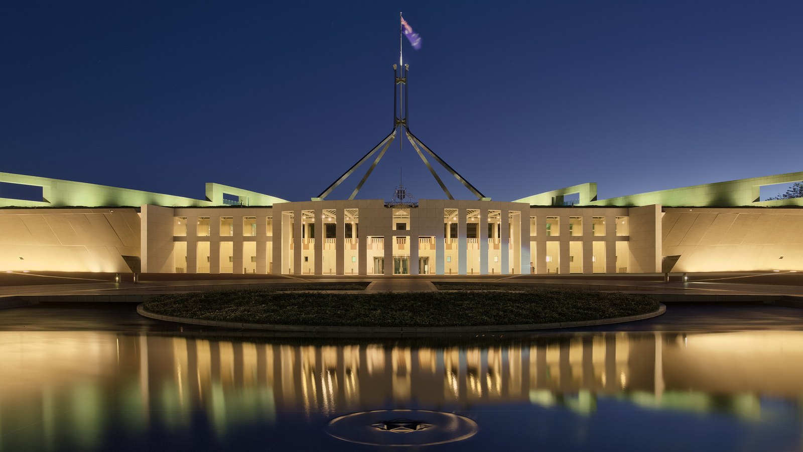 Australian Parliament House in Canberra illuminated at dusk and reflected in a pool.