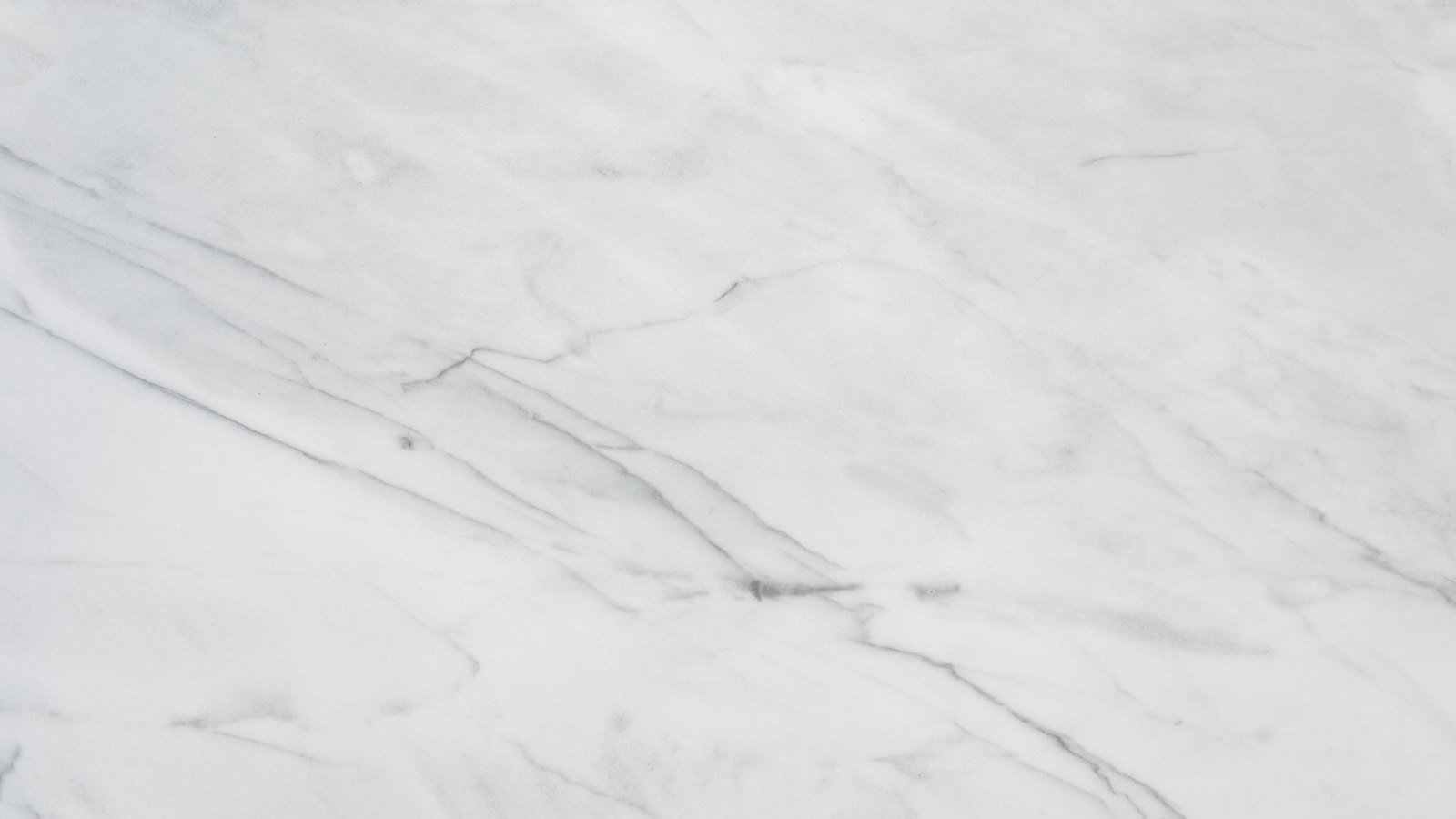 A close photograph of white marble filling the frame, fine grey veins running diagonally across the pale stone and branching away into hairline threads, with faint cloudy shading between them. No text, marking, object, person or edge is in view.