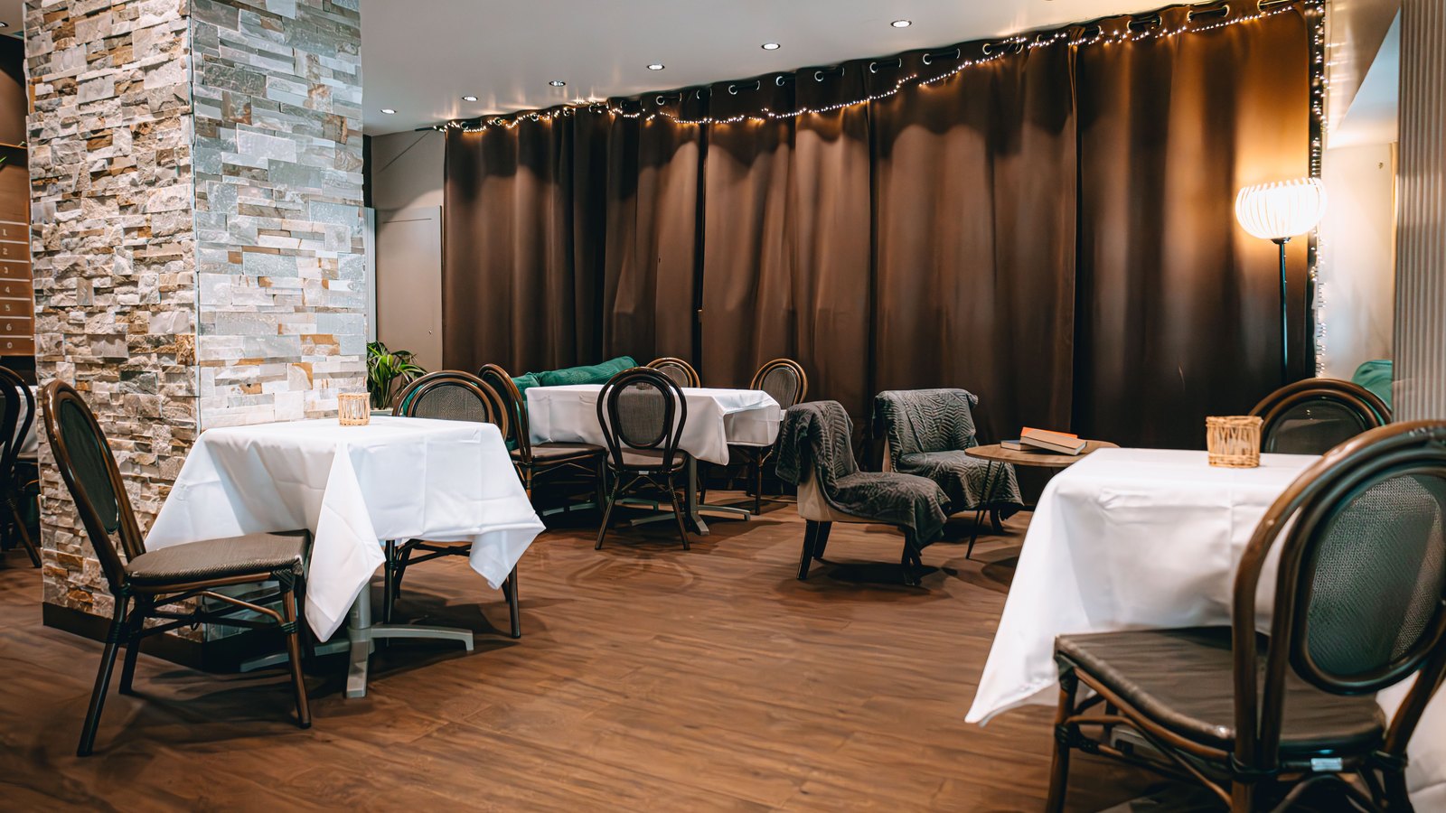 An empty restaurant dining room with white tablecloths, dark chairs and warm ceiling lights. No person, brand, sign or readable text appears. A stock photograph, not a photograph of this event.