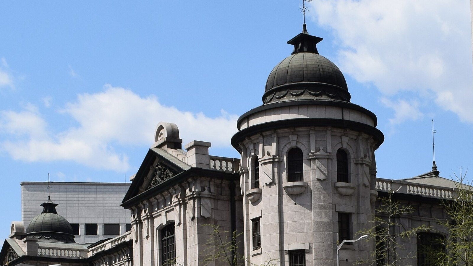 The domed corner tower and stone facade of the Bank of Korea's former head office in Seoul, now its money museum, with a second smaller dome and a pediment against a blue sky with light cloud.