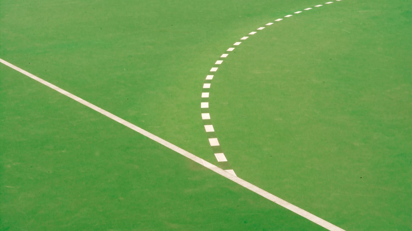A close overhead photograph of a flat green playing surface marked with a solid white painted line running corner to corner and a dashed white arc curving away from it. No people, players, equipment, buildings, signage, lettering or logos are in the frame, and no place, sport or school is identifiable. A generic illustration of pitch markings, not a photograph of Barron Collier High School or of any Collier County field.