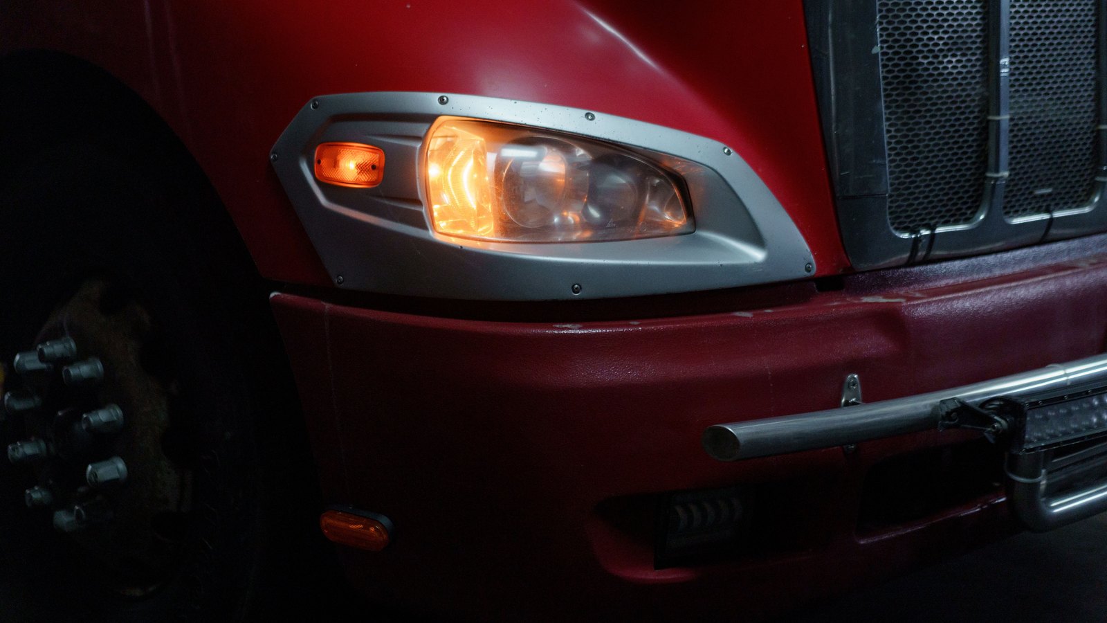 The illuminated headlight and amber marker light of a red truck in darkness, not a photograph of this event.
