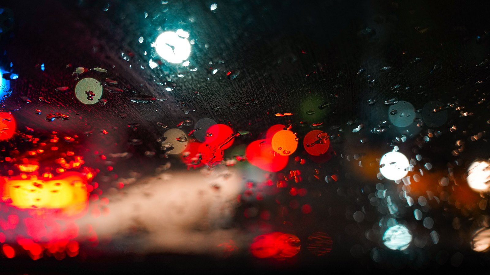 Blurred red, white and blue road lights seen through a rain-covered windshield, not a photograph of this event.