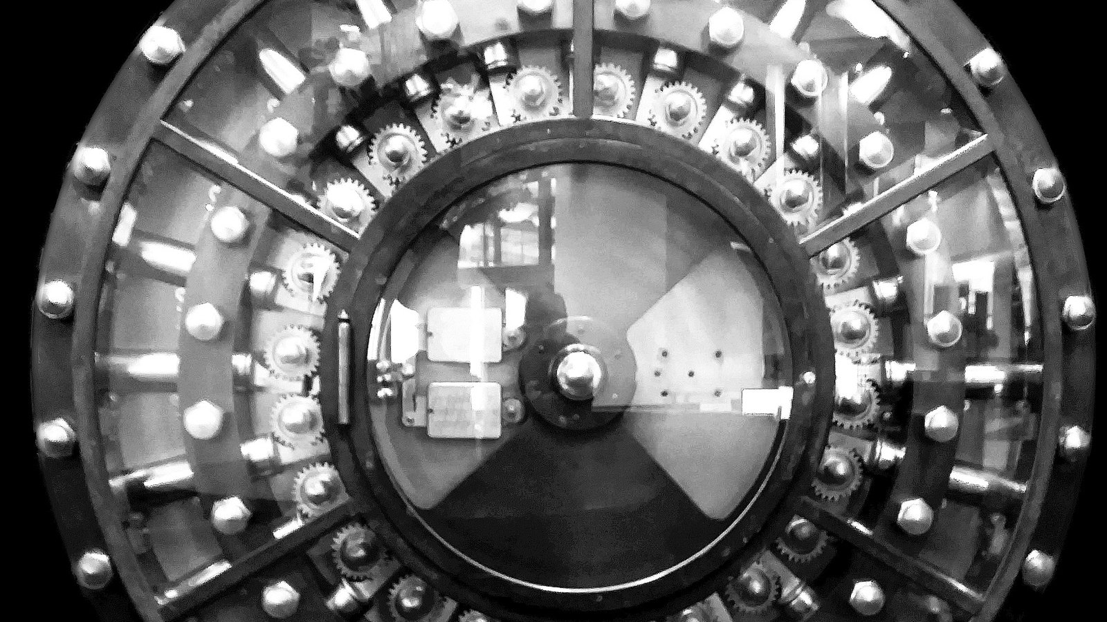 A circular steel bank vault door with its locking mechanism exposed.