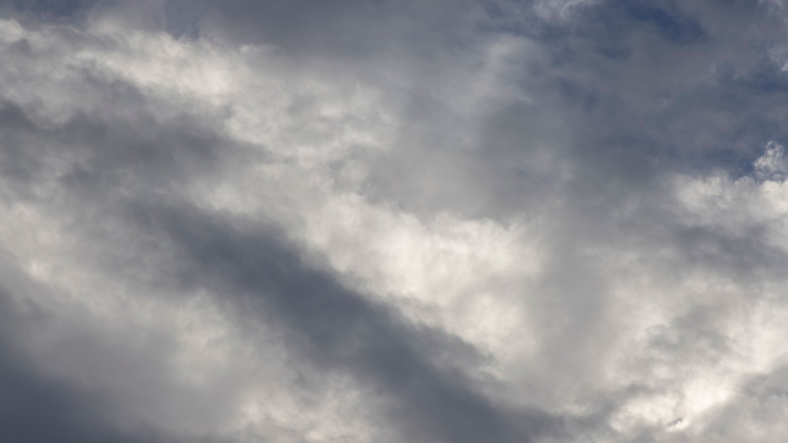 A photograph of grey and white cloud filling the frame, with a diagonal band of darker shadow across the middle and a few patches of pale blue sky showing through at the top and right, used as an illustration. It is not a photograph of this crash or of the Six Mile Cypress corridor.