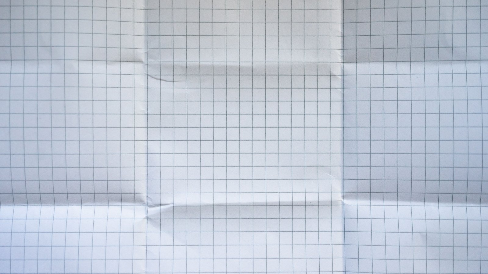 A sheet of pale blue graph paper filling the whole frame, blank, with the creases from being folded and reopened still running across it.