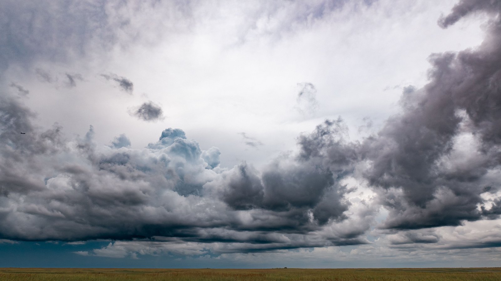 Dark storm clouds build over a flat grassland, not a photograph of either storm in the Weather Service statements.