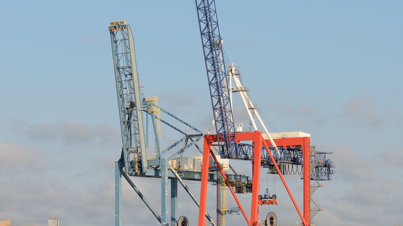 The upper structures of two container gantry cranes at a New York terminal standing against a pale sky, booms raised, with no vessel, lettering or person in the frame.