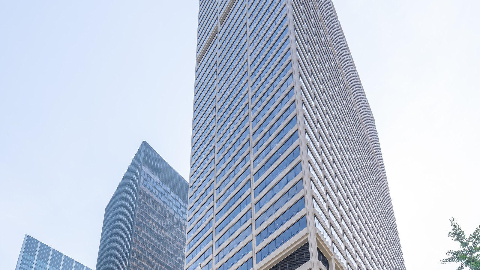 Looking up at a tall pale stone and glass office tower on Park Avenue in Manhattan, with a darker glass tower beside it against a hazy sky.