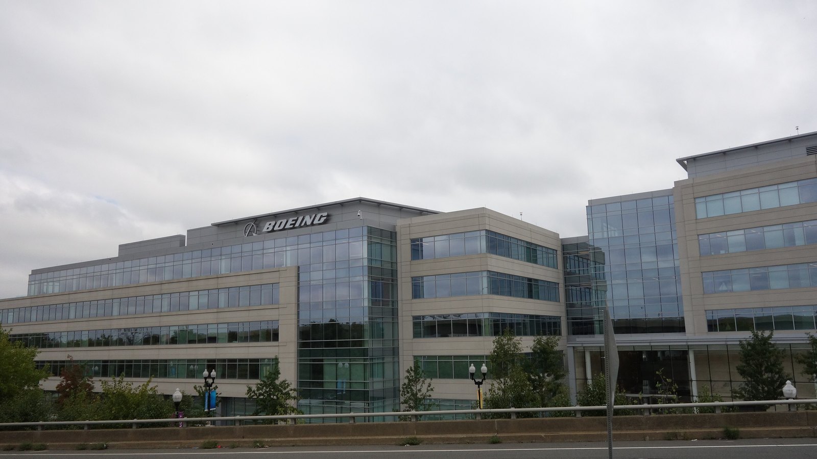 A low office block in Virginia with a glass and stone facade, the Boeing name and symbol mounted along its roofline, photographed from the road under an overcast sky.