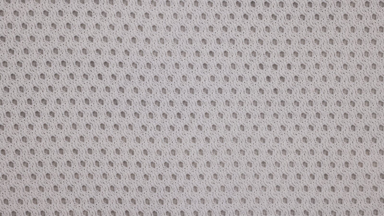 An off-white spacer mesh knit fabric photographed square on and filling the whole frame, an even grid of small rounded openings running edge to edge with the darker layer behind showing through each one. The looped yarn between the holes is slightly irregular. No text, brand mark, person or place is in view.