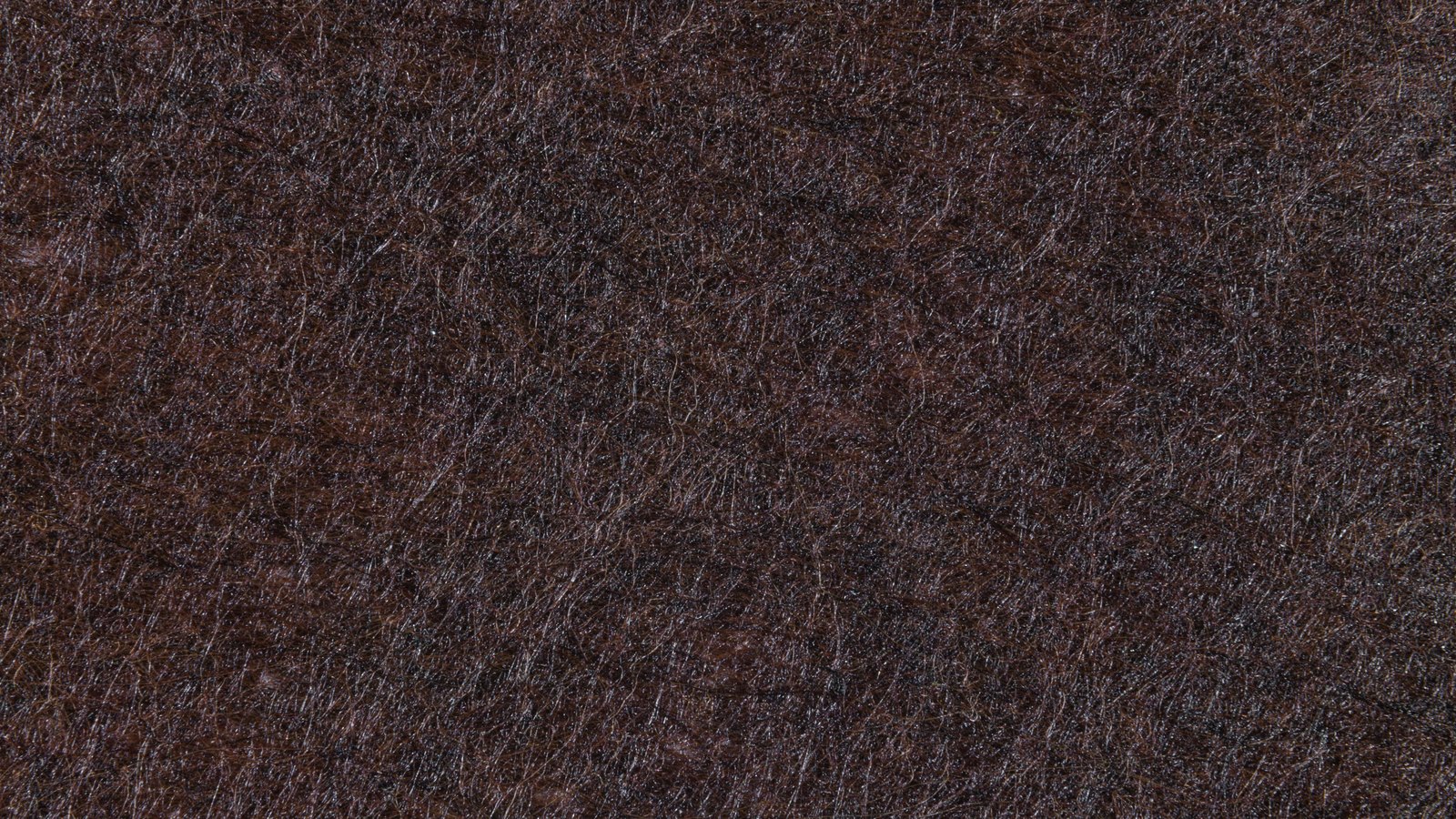 A full frame macro of a dark brown matted fibre surface, its short fibres lying every which way and catching small points of light right across the picture. No object, person, place, lettering or brand mark is in view.