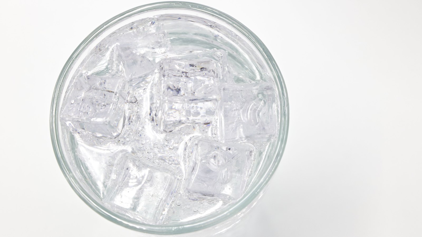 Looking straight down into a plain drinking glass filled with clear water and ice cubes, against a white background. No people, signage, lettering or brand marks are visible and no place can be identified from it. A generic household illustration, not a photograph of Bokeelia, of Pine Island or of anyone's tap water.