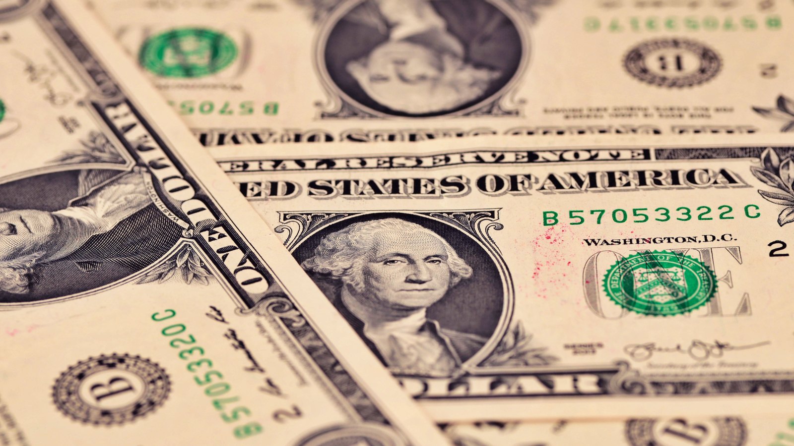 A close overlapping arrangement of United States one dollar bills showing the Federal Reserve note face and Treasury seal.