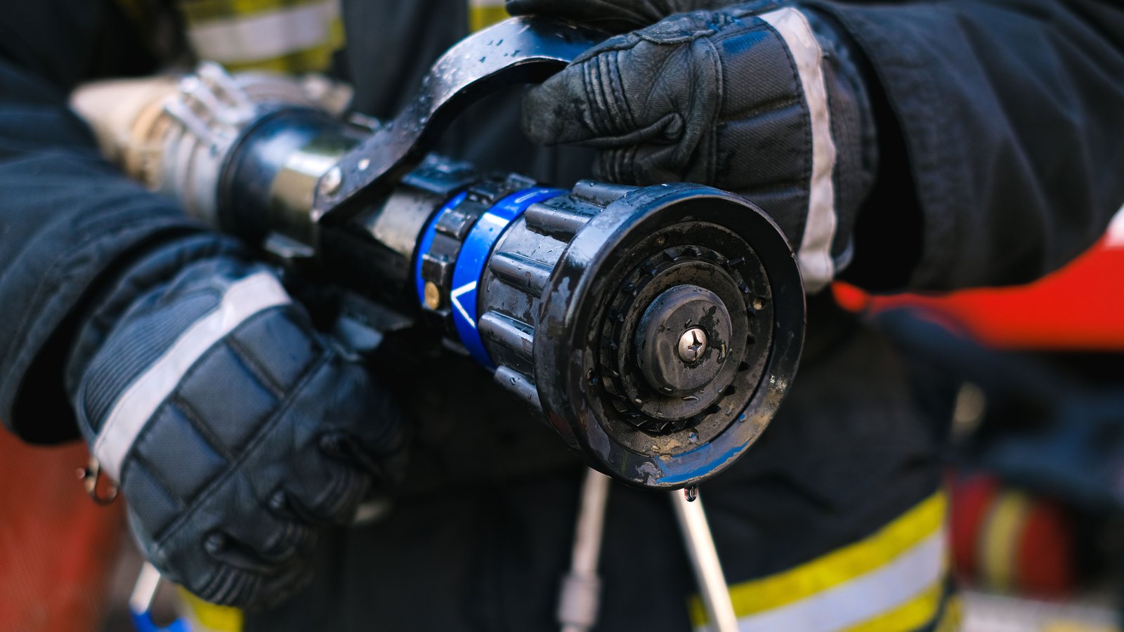 A tight crop on two gloved hands in dark turnout gear with reflective striping, gripping the blue and black nozzle of a charged fire hose. No face, vehicle, building, signage, unit number or lettering of any kind appears in the frame. Stock photograph, not a photograph of this event.