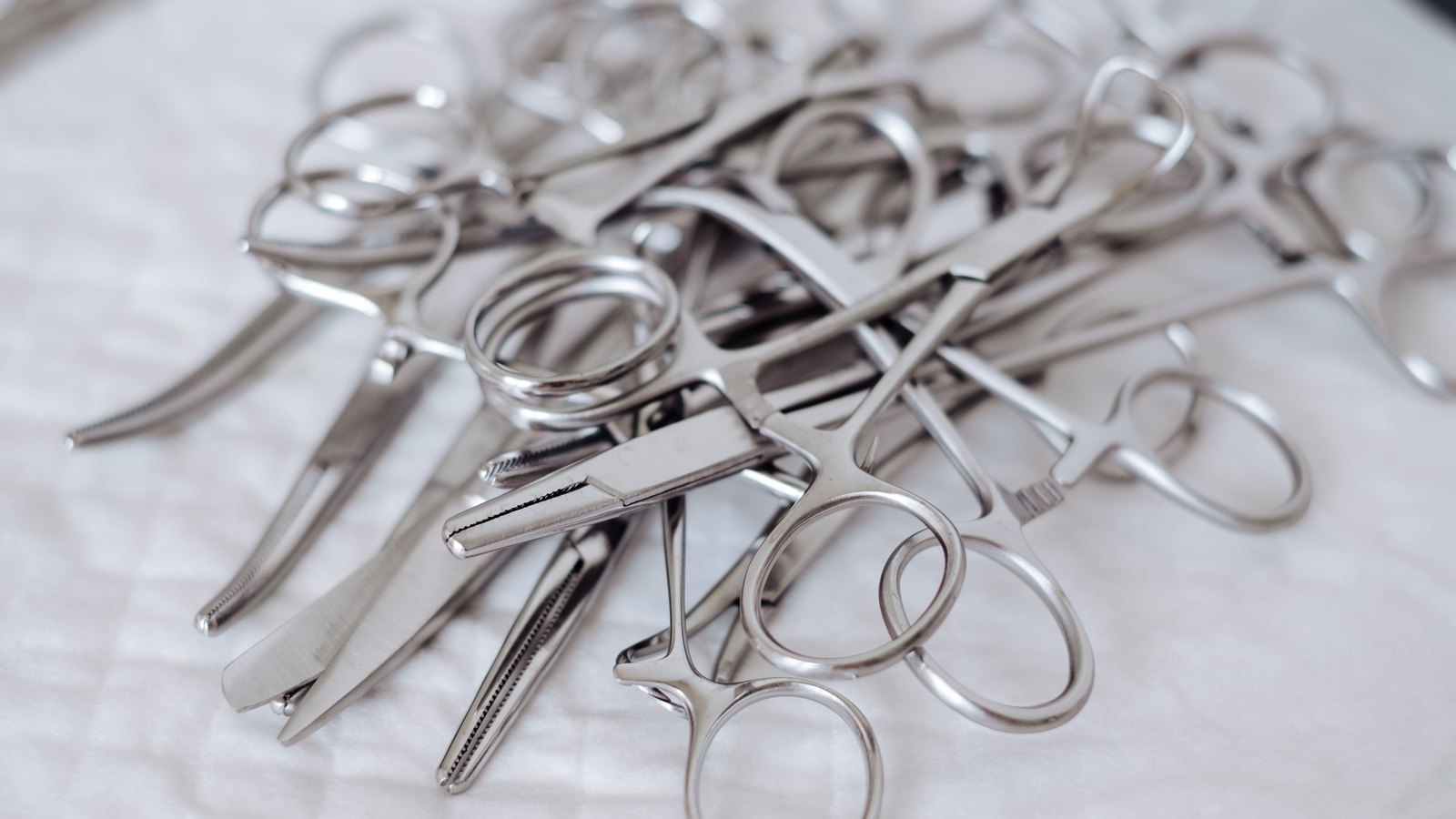 A loose pile of stainless steel surgical clamps and scissors lying on a white cloth, shot close and from the side, with no packaging, no markings and no hands in the frame.