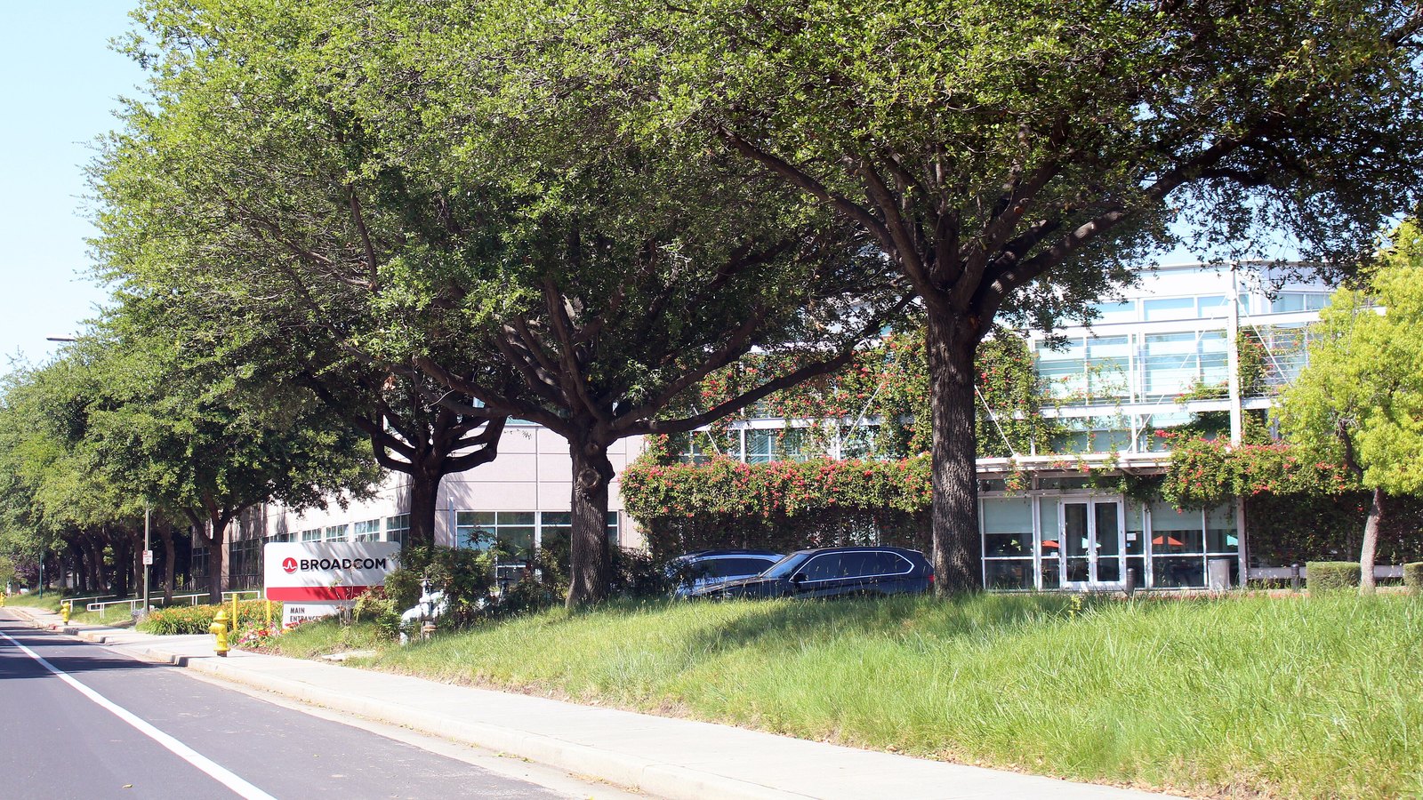 Broadcom's San Jose headquarters behind mature trees, with its name on the entrance sign.