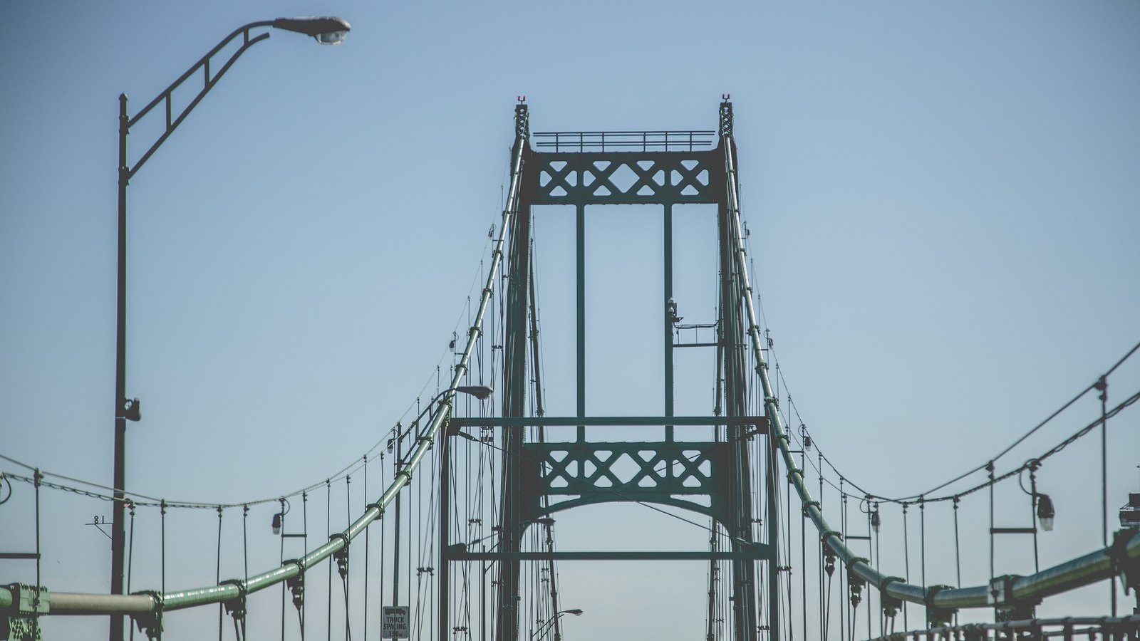 The steel tower and suspension cables of the Thousand Islands Bridge, which carries the international crossing between Ontario and New York, seen head on from the deck against a pale sky.