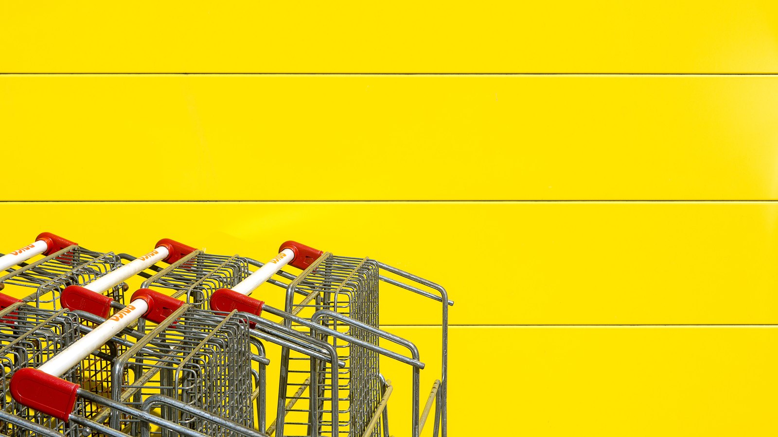 A row of empty shopping carts against a bright yellow retail wall; illustrative.