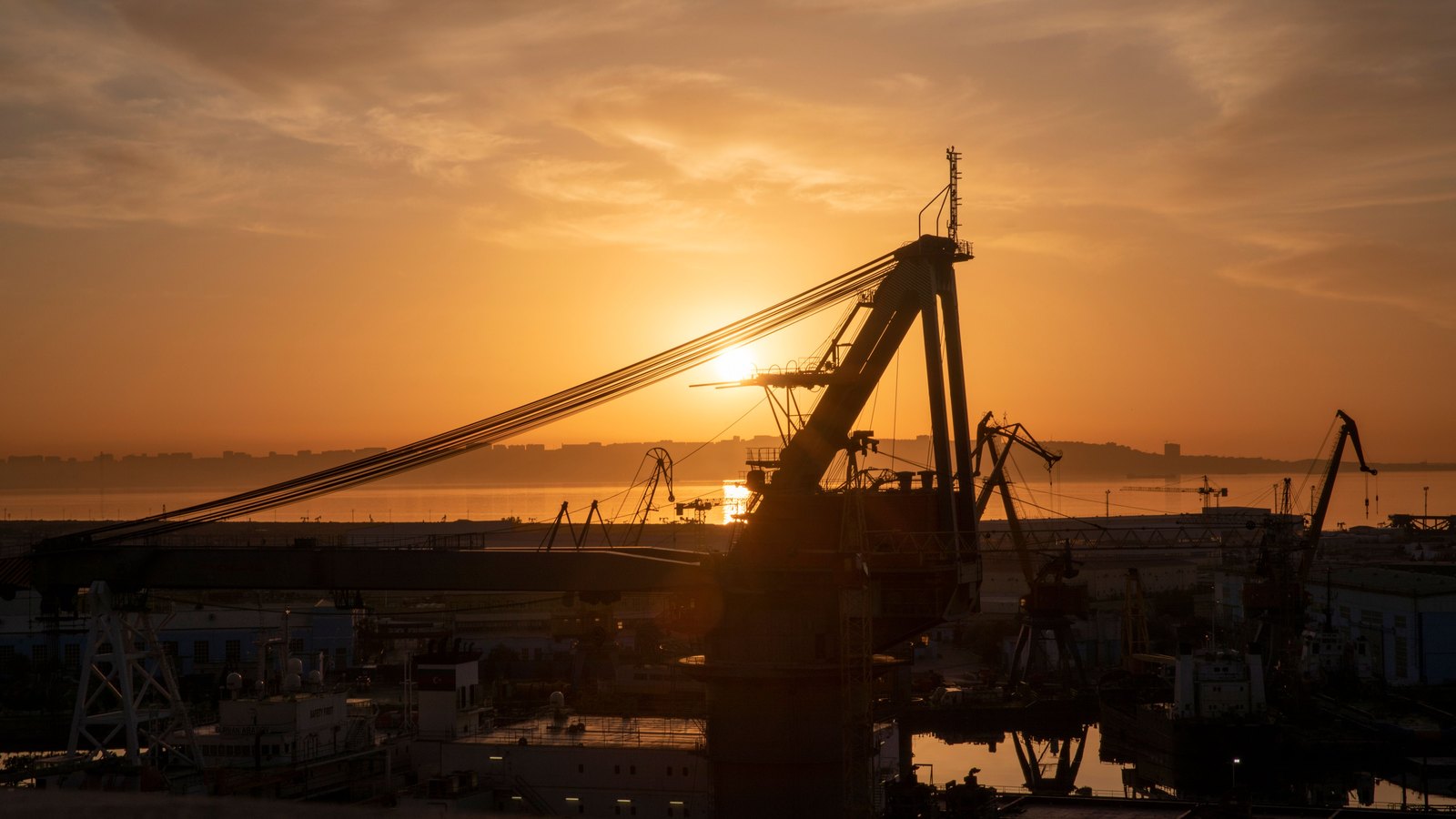 Cargo handling cranes silhouetted at a port during sunrise, illustrating the movement of tariffed goods.