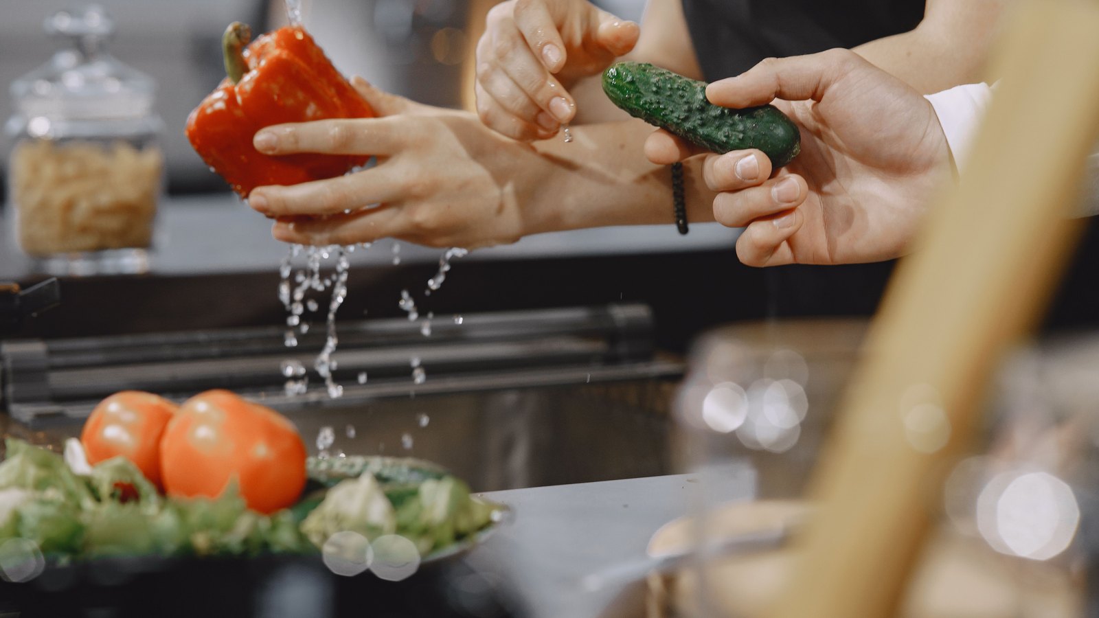 Hands wash fresh vegetables under running water at a kitchen faucet, not a photograph of this advisory.