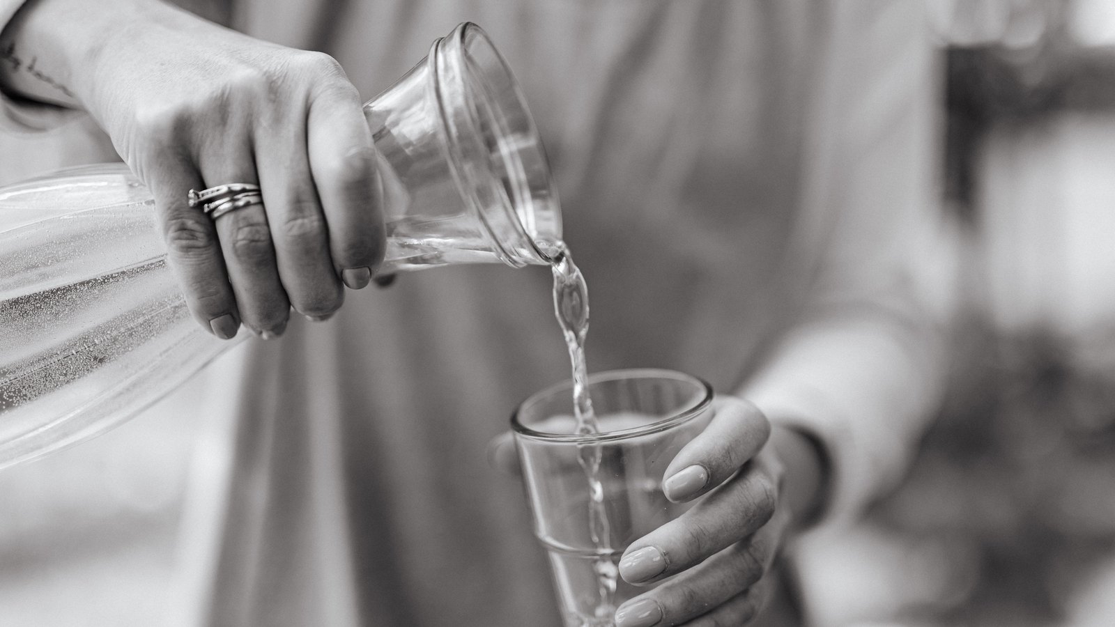 Hands pour clear water from a glass carafe into a drinking glass, not a photograph of this advisory.