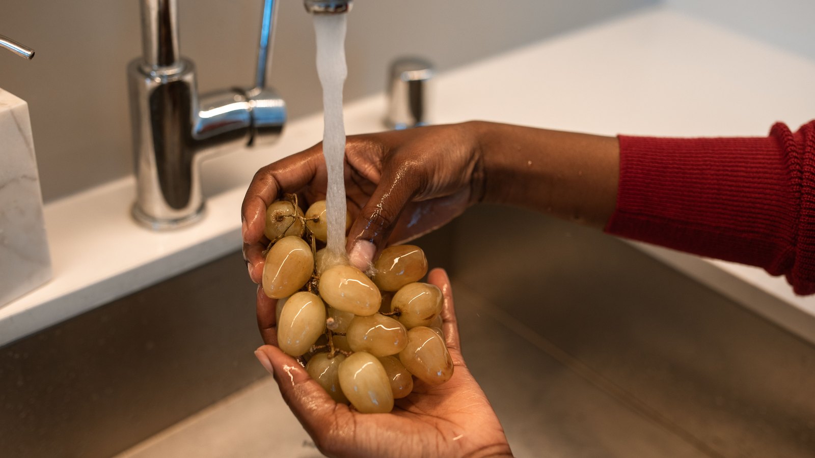 Hands wash green grapes under running water at a kitchen faucet, not a photograph of this advisory.
