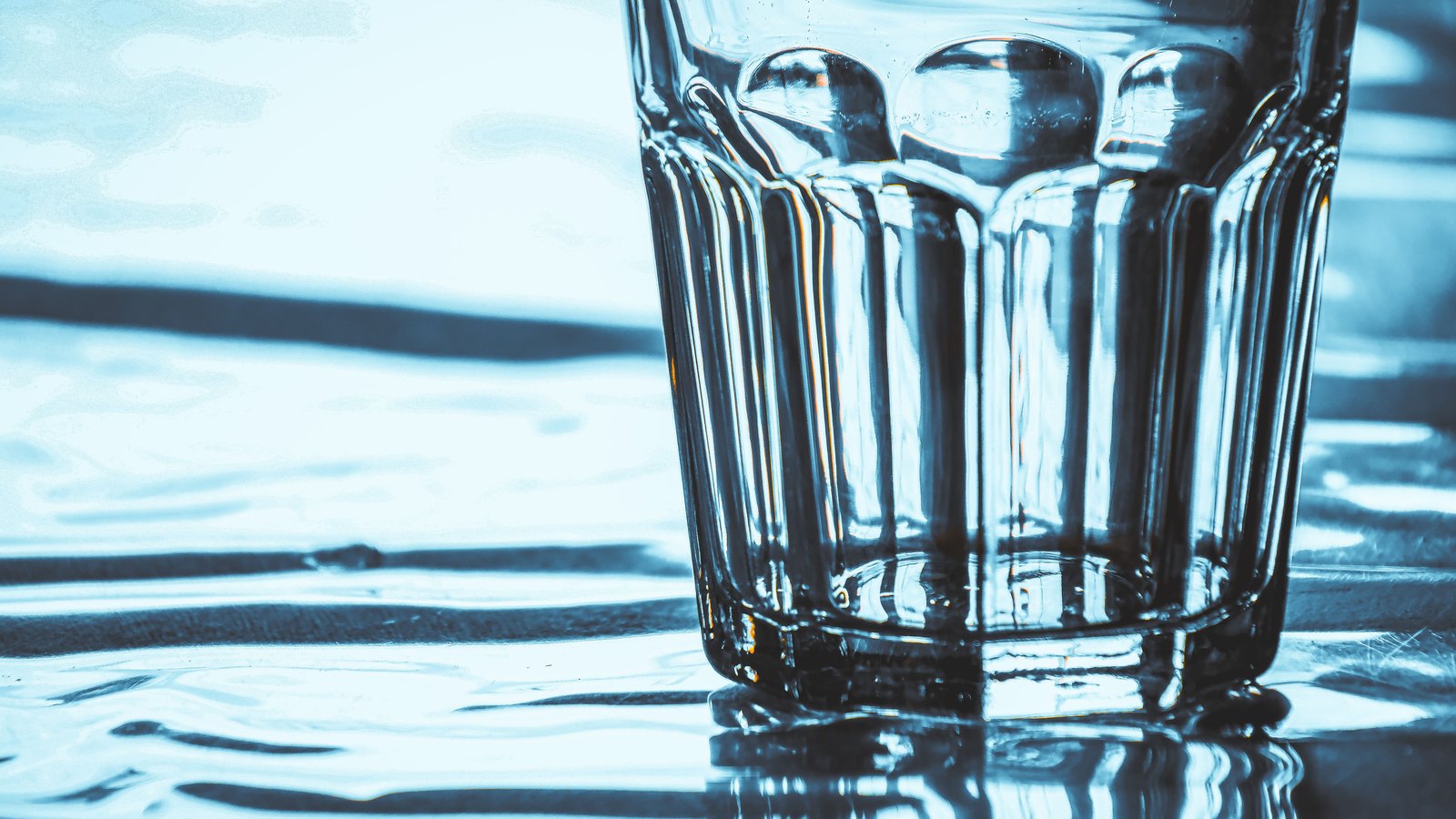 Close view of a clear drinking glass on a blue reflective surface, not a photograph of this event.