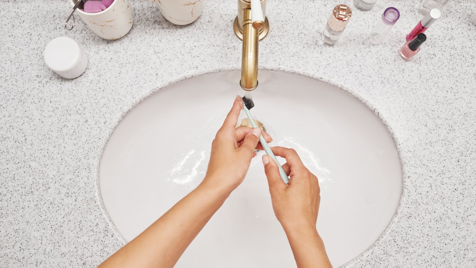 Hands rinse a toothbrush under a running bathroom faucet, not a photograph of this event.