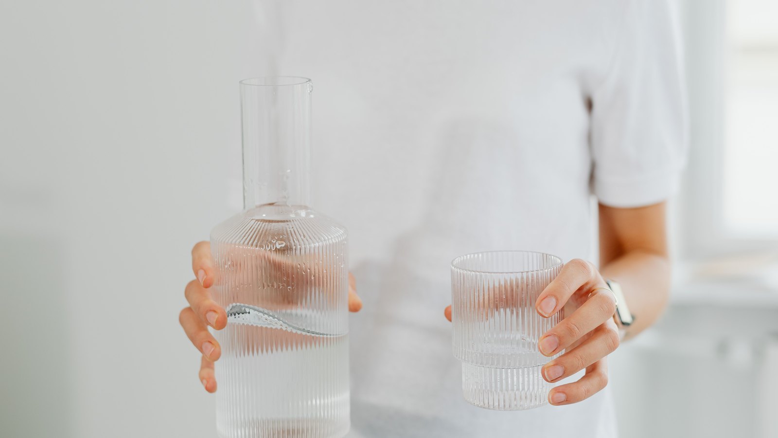 Hands hold a ribbed glass carafe and a drinking glass filled with clear water, not a photograph of this advisory.