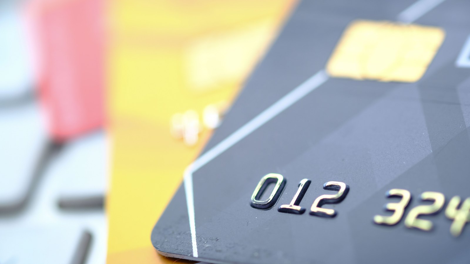 A close-up of a dark grey payment card showing its embossed account digits and gold chip, resting on a yellow card.