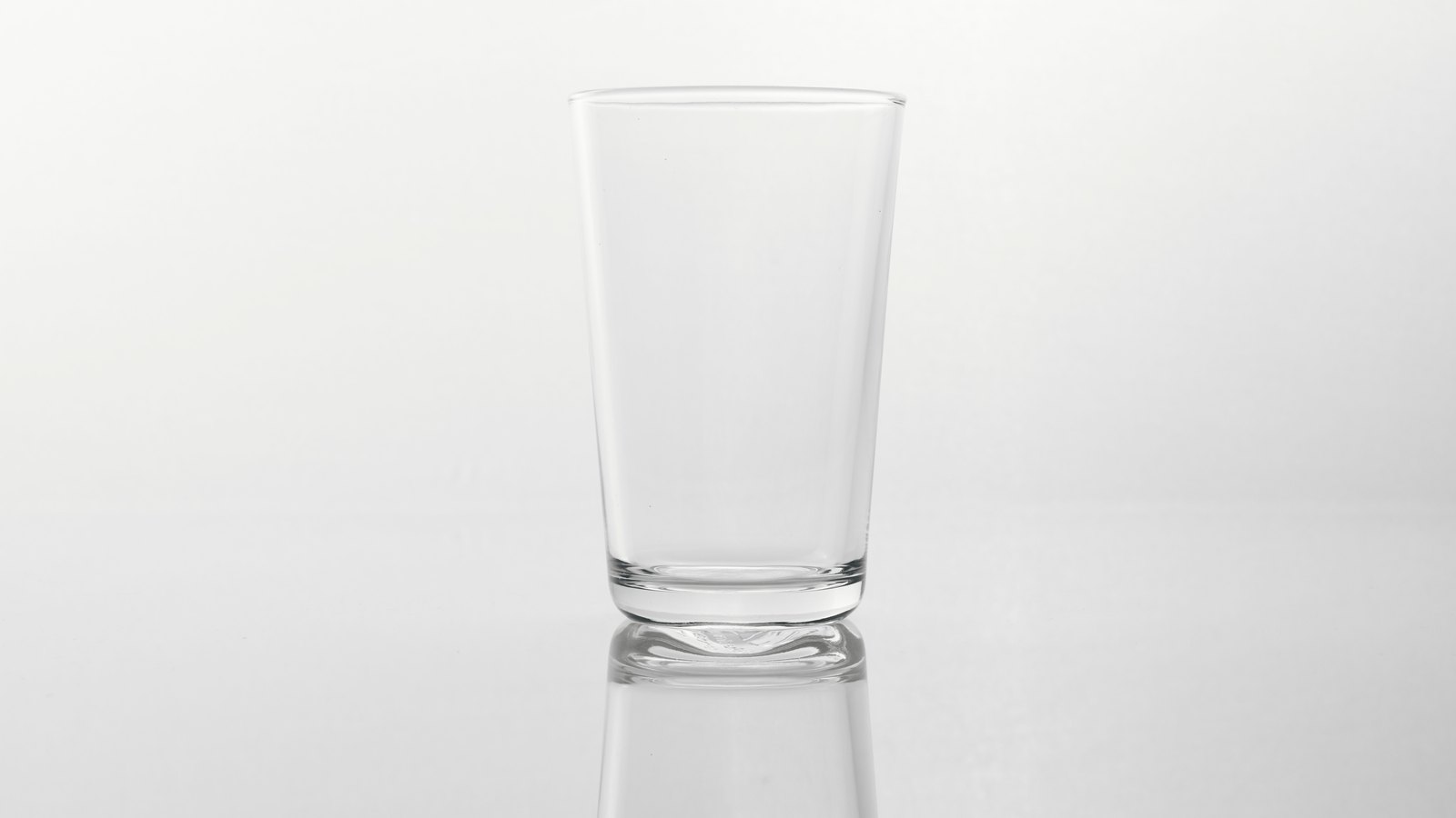 A single plain drinking glass, clear and unmarked, standing empty on a white reflective surface against a plain white background. The glass holds no water. There is no text, signage, brand mark, person, hand, food or identifiable place in the frame. A generic illustration of a drinking glass, not a photograph of Cape Coral, of any water main break or of anyone's tap, and not evidence about the condition of anyone's water. Its weakness is stated rather than glossed: the glass is empty, so the picture does not show the boiled or bottled water the notice tells residents to use, and an empty glass should not be read as a claim that anyone has no water.