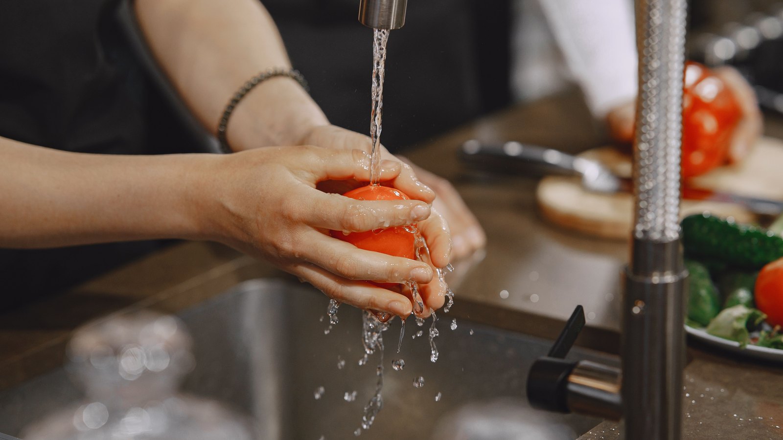 Hands washing a tomato beneath a running kitchen faucet, not a photograph of this event.
